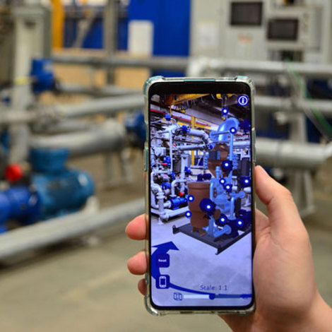 Hand holding smartphone displaying augmented reality in industrial setting with machinery.