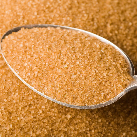 Spoonful of brown sugar granules on a pile of loose sugar crystals.