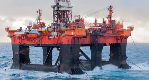 Offshore oil rig platform in the ocean, with waves crashing against its structure.